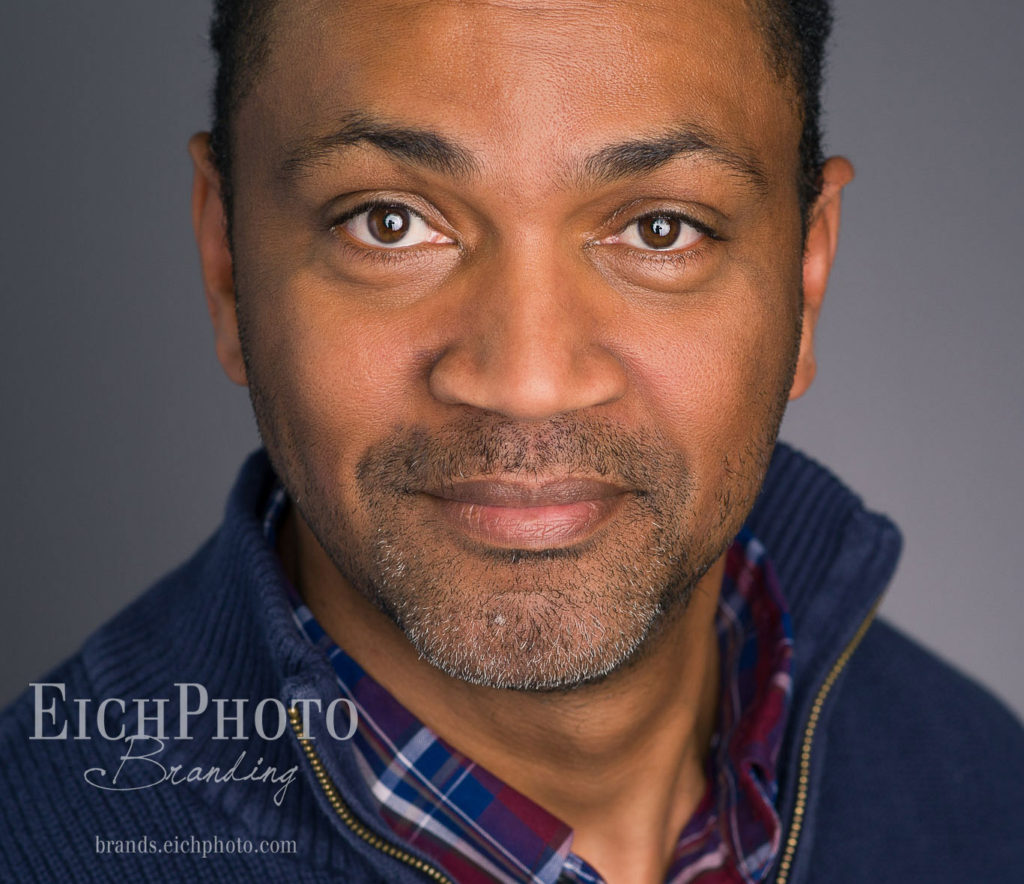 Handsome Black African American gentleman smiles slightly at the camera, gives genuine helpful look with his eyes. Realtor convention conference headshot. Eichelberger Photography