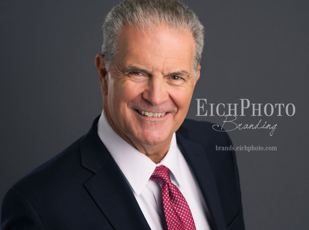 Smiling Friendly Bank President In black suit and red tie, grey hair, professional headshot
